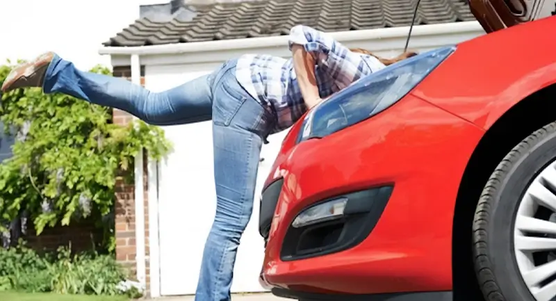 a picture of a man in jeans leaning over the engine of a red sports car with its hood up